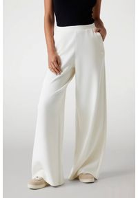 Guess - GUESS Spodnie damskie dresowe ecru Olympe Wide. Kolor: biały. Materiał: dresówka