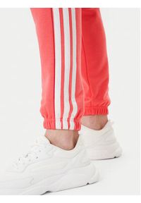 Adidas - adidas Spodnie dresowe Essentials 3-Stripes KE4387 Koralowy Regular Fit. Kolor: pomarańczowy. Materiał: bawełna