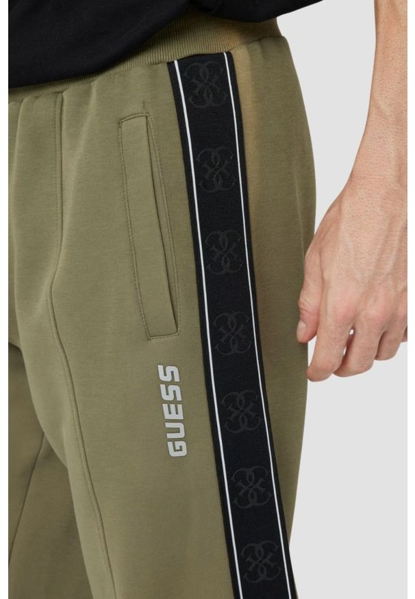 Guess - GUESS Zielone męskie spodnie dresowe z lampasami Mickey. Kolor: zielony. Materiał: dresówka