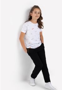 Volcano - Dziewczęca koszulka z wydłużonym tyłem T-LOOK JUNIOR. Kolor: biały. Materiał: bawełna. Długość rękawa: krótki rękaw. Długość: krótkie. Wzór: nadruk. Sezon: lato