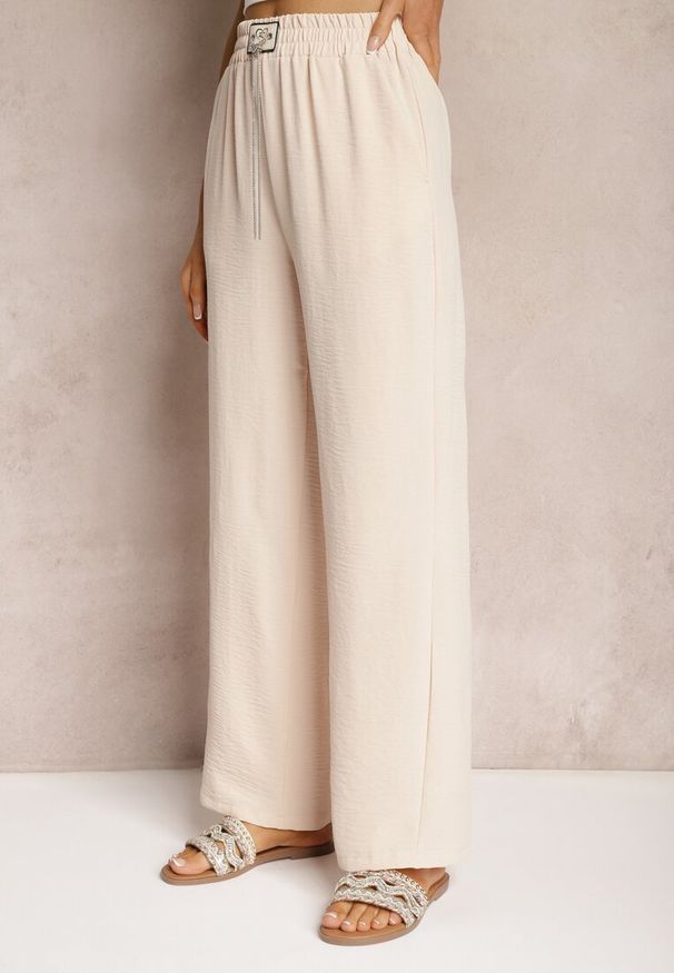 Renee - Beżowe Spodnie Luźne o Szerokich Nogawkach z Łańcuszkiem zamiast Troczka Ostaria. Okazja: na spotkanie biznesowe, do pracy. Stan: podwyższony. Kolor: beżowy. Wzór: aplikacja. Styl: biznesowy