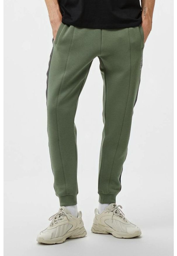 Guess - GUESS Zielone męskie spodnie dresowe z lampasami Mickey, Rozmiar XL. Kolor: zielony. Materiał: dresówka