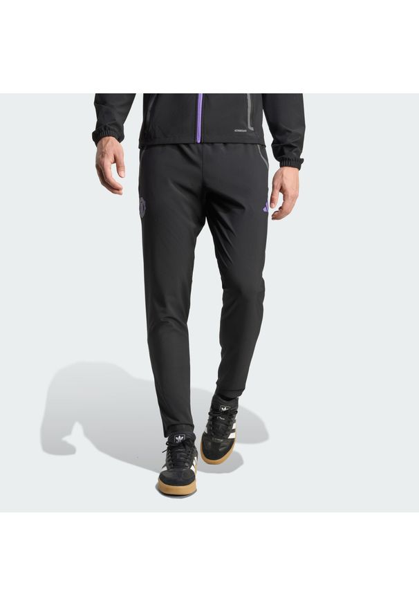 Adidas - Spodnie Manchester United Tiro 25 Competition Vis Tech Travel. Kolor: fioletowy, wielokolorowy, czarny. Sport: piłka nożna