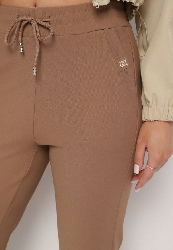Born2be - Brązowe Szerokie Spodnie z Wiązaniem i Metalicznymi Aplikacjami Mairae. Okazja: na co dzień. Kolor: brązowy. Wzór: aplikacja. Styl: casual, elegancki