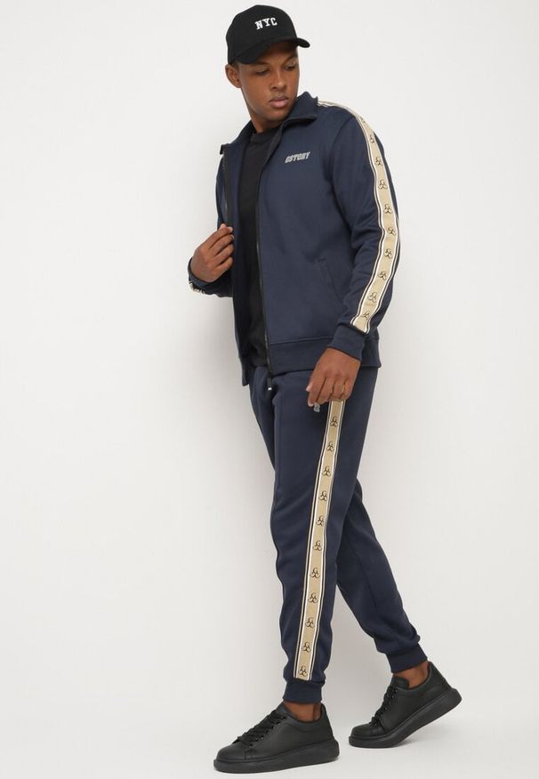 Born2be - Granatowe Spodnie Dresowe ze Ściągaczem Zdobione Lampasem z Polarową Podszewką Edittia. Okazja: na co dzień. Kolor: niebieski. Materiał: polar, dresówka. Wzór: aplikacja. Styl: elegancki, casual, klasyczny