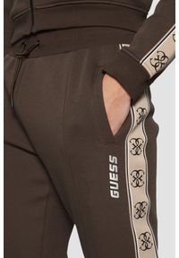 Guess - GUESS Brązowe męskie spodnie dresowe z lampasami Mickey. Kolor: brązowy. Materiał: dresówka #3