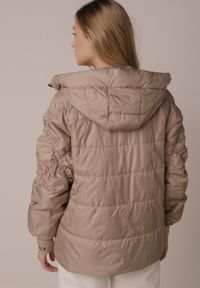 Born2be - Ciemnobeżowa Przejściowa Kurtka Pikowana z Kapturem i Napisami na Rękawach Althone. Okazja: na co dzień. Typ kołnierza: kaptur. Kolor: beżowy. Materiał: poliester. Wzór: napisy. Styl: casual #8