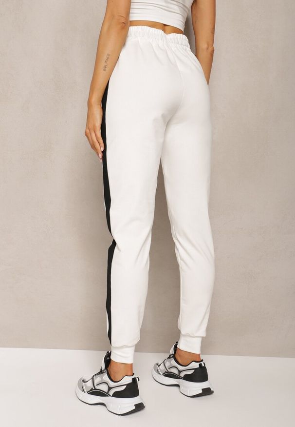 Renee - Białe Spodnie Dresowe High Waist Wykończone Lampasami i Ozdobione Napisem Sikara. Okazja: na co dzień. Stan: podwyższony. Kolor: biały. Materiał: dresówka. Długość: krótkie. Wzór: aplikacja, napisy. Styl: sportowy, casual, elegancki