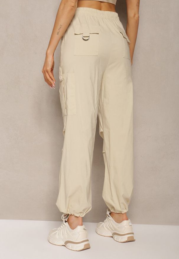 Renee - Jasnobeżowe Szerokie Spodnie High Waist w Stylu Bojówek Wykończone Gumką w Talii Ellcara. Okazja: na co dzień. Stan: podwyższony. Kolor: beżowy. Materiał: satyna. Wzór: moro. Styl: militarny, elegancki, casual, wizytowy, sportowy