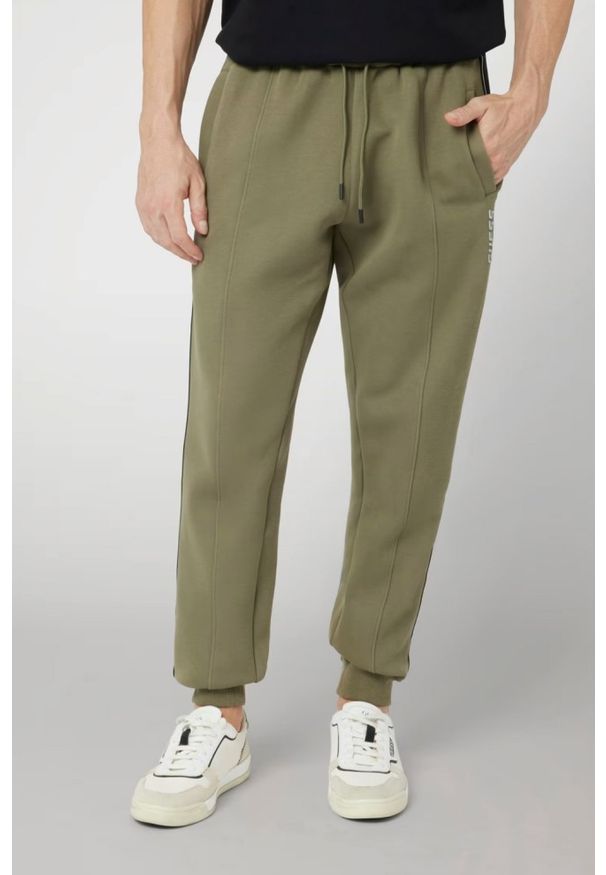 Guess - GUESS Zielone męskie spodnie dresowe z lampasami Mickey, Rozmiar XL. Kolor: zielony. Materiał: dresówka