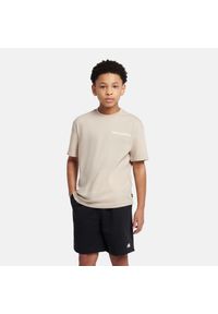 Koszulka dziecięca New Balance YT61A21ATWF – beżowa. Kolor: beżowy. Materiał: materiał, bawełna. Długość rękawa: krótki rękaw. Długość: krótkie. Wzór: aplikacja #1