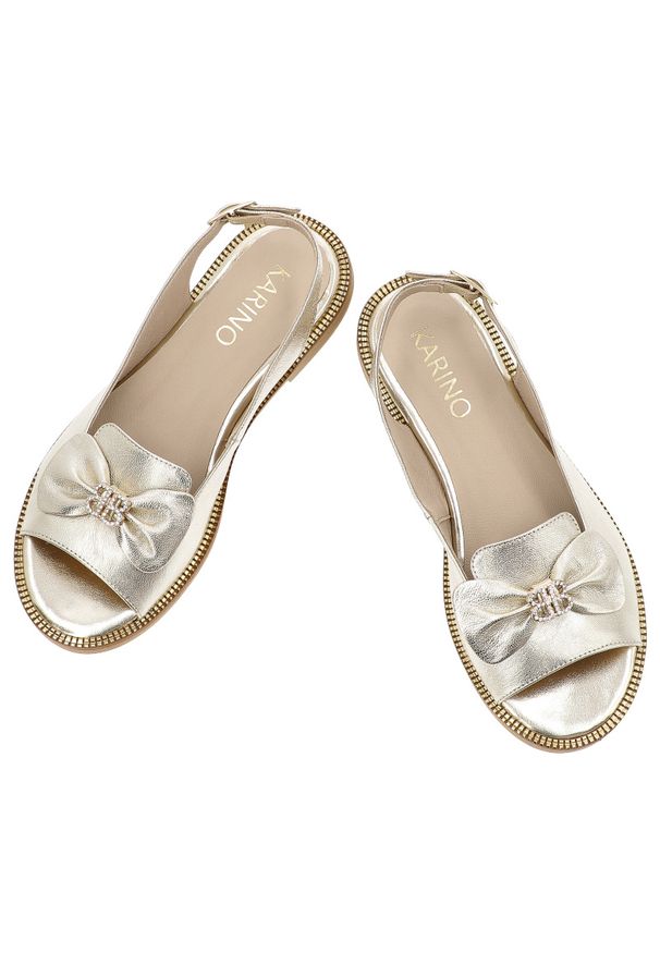 Złote Sandały Karino Modne Obuwie Damskie Z Broszką. Nosek buta: otwarty. Zapięcie: pasek. Kolor: złoty. Materiał: skóra. Wzór: aplikacja. Sezon: lato. Obcas: na płaskiej podeszwie. Styl: klasyczny, elegancki