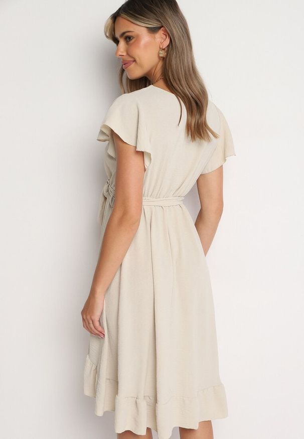 Born2be - Beżowa Kopertowa Sukienka z Asymetrycznym Dołem Ozdobiona Falbanką z Paskiem w Talii Snidia. Okazja: na co dzień, na spacer. Kolor: beżowy. Wzór: aplikacja. Sezon: lato. Typ sukienki: asymetryczne, kopertowe. Styl: klasyczny, casual, elegancki