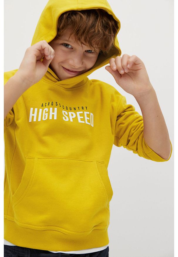 Mango Kids - Bluza bawełniana dziecięca 110-164 cm. Okazja: na co dzień. Typ kołnierza: kaptur. Kolor: żółty. Materiał: bawełna. Wzór: nadruk. Styl: casual