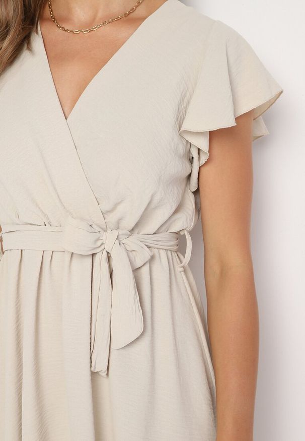 Born2be - Beżowa Kopertowa Sukienka z Asymetrycznym Dołem Ozdobiona Falbanką z Paskiem w Talii Snidia. Okazja: na spacer, na co dzień. Kolor: beżowy. Wzór: aplikacja. Sezon: lato. Typ sukienki: kopertowe, asymetryczne. Styl: elegancki, casual, klasyczny