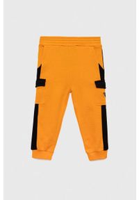 Guess spodnie dresowe bawełniane dziecięce kolor pomarańczowy wzorzyste. Stan: podwyższony. Kolor: pomarańczowy. Materiał: bawełna, dresówka