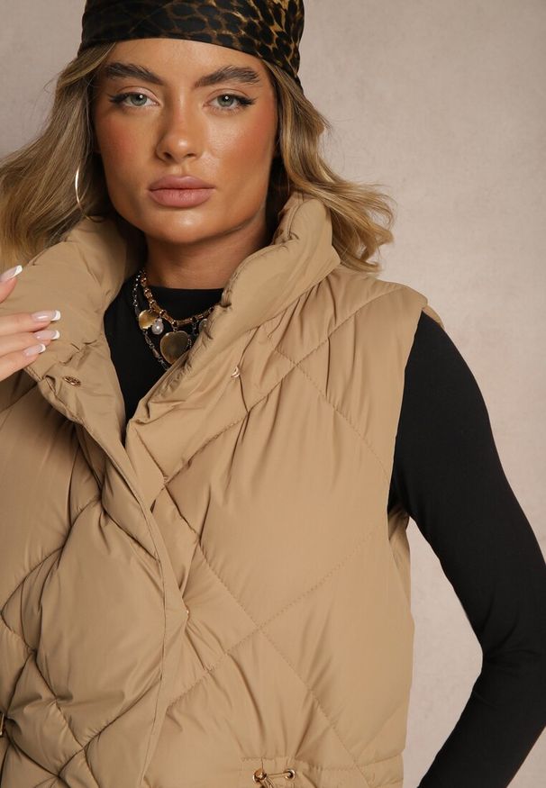 Renee - Ciemnobeżowa Długa Kamizelka z Pikowanymi Przeszyciami ze Stójką i Kieszeniami Avalithe. Okazja: na co dzień, na spacer. Typ kołnierza: kołnierzyk stójkowy. Kolor: beżowy. Materiał: jeans. Długość: długie. Styl: sportowy, casual, elegancki