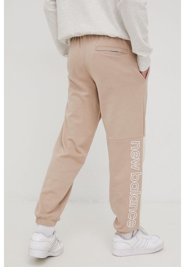 New Balance spodnie dresowe bawełniane MP21550MDY męskie kolor beżowy z nadrukiem. Kolor: beżowy. Materiał: bawełna, dresówka. Wzór: nadruk
