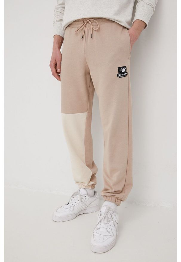 New Balance spodnie dresowe bawełniane męskie kolor beżowy z nadrukiem. Kolor: beżowy. Materiał: dresówka, bawełna. Wzór: nadruk