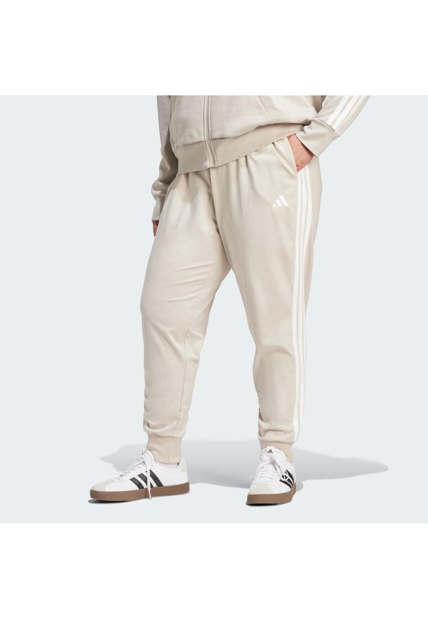 Adidas - Spodnie Dresowe Essentials 3-Stripes (Dla Sylwetek Plus Size). Kolekcja: plus size. Kolor: beżowy, wielokolorowy, biały. Materiał: dresówka. Sport: fitness