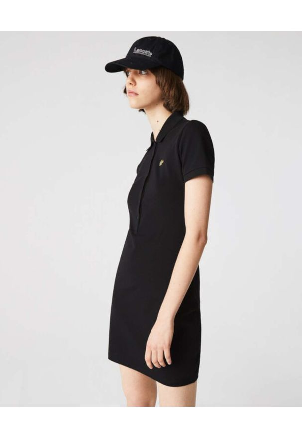 Lacoste - LACOSTE - Czarna sukienka z metalowym logo Slim Fit. Typ kołnierza: polo. Kolor: czarny. Materiał: prążkowany, materiał. Wzór: aplikacja. Styl: klasyczny. Długość: mini