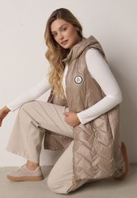 Born2be - Brązowa Przejściowa Kamizelka Pikowana o Długim Kroju z Kapturem i Naszywką Harmaste. Okazja: na co dzień. Typ kołnierza: kaptur. Kolor: brązowy. Materiał: jeans. Długość: długie. Wzór: aplikacja. Styl: casual #1