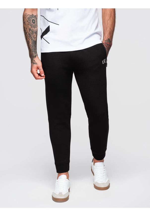 Ombre Clothing - Spodnie dresowe męskie ze ściągaczami w nogawkach i gumowym nadrukiem – czarne V1. Kolor: czarny. Materiał: guma, dresówka. Wzór: nadruk. Styl: sportowy, elegancki