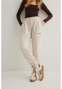 Marsala - Spodnie typu jogger w kolorze LATTE MELANGE - AUSTIN. Stan: podwyższony. Materiał: dzianina, bawełna, poliester, dresówka. Wzór: haft, melanż, aplikacja. Styl: elegancki