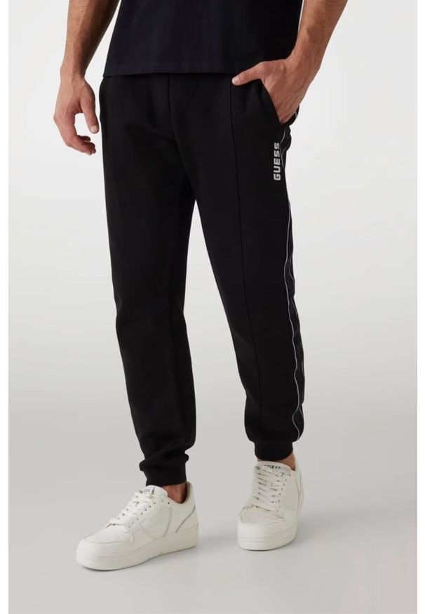 Guess - GUESS Czarne męskie spodnie dresowe z lampasami Mickey, Rozmiar L. Kolor: czarny. Materiał: dresówka