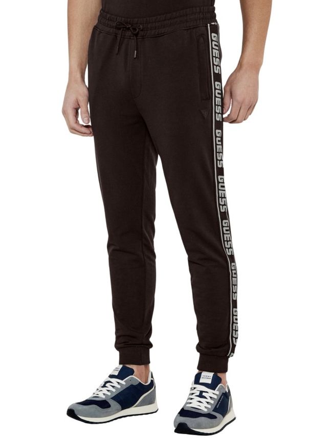 Guess - GUESS Brązowe męskie spodnie dresowe z lampasami New Arlo. Kolor: brązowy. Materiał: dresówka