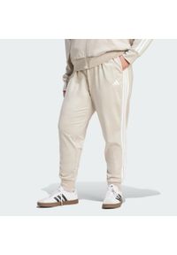 Adidas - Spodnie Dresowe Essentials 3-Stripes (Dla Sylwetek Plus Size). Kolekcja: plus size. Kolor: beżowy, wielokolorowy, biały. Materiał: dresówka. Sport: fitness #1