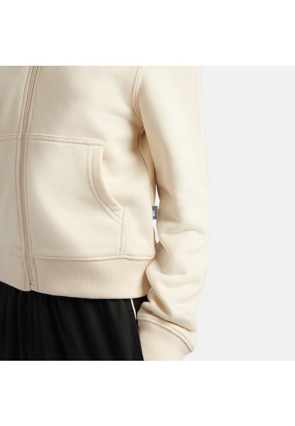 Bluza dziecięca New Balance YT61P93CLIN – beżowa. Kolor: beżowy. Materiał: materiał, bawełna, poliester. Wzór: napisy, aplikacja. Styl: sportowy