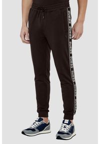 Guess - GUESS Brązowe męskie spodnie dresowe z lampasami New Arlo. Kolor: brązowy. Materiał: dresówka