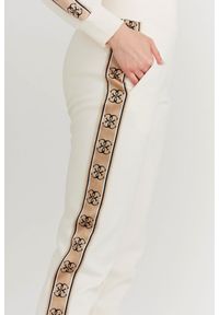 Guess - GUESS Kremowe spodnie damskie z lampasami w logo. Kolor: kremowy. Materiał: bawełna. Wzór: aplikacja