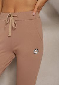 Renee - Ciemnobeżowe Spodnie Dresowe Ozdobione Małą Naszywką Nulorea. Kolor: beżowy. Materiał: dresówka. Długość: długie. Wzór: aplikacja #3