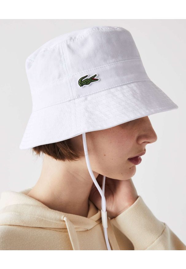 Lacoste - LACOSTE - Biały kapelusz typu bucket ze ściągaczem. Kolor: biały. Materiał: bawełna. Wzór: haft