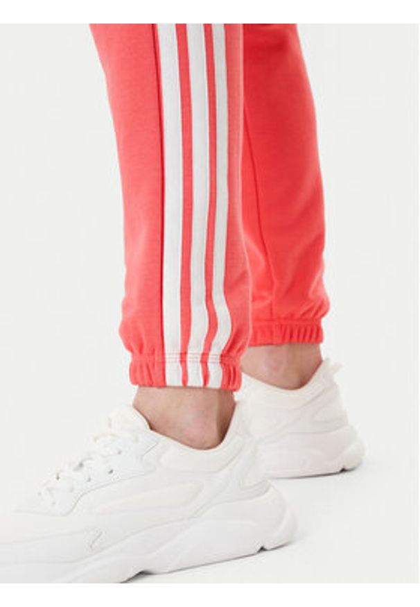 Adidas - adidas Spodnie dresowe Essentials 3-Stripes KE4387 Koralowy Regular Fit. Kolor: pomarańczowy. Materiał: bawełna