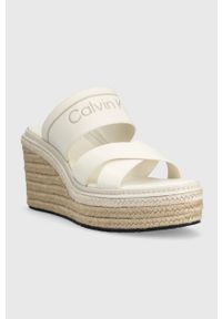 Calvin Klein klapki WEDGE 50HH - HE damskie kolor biały na koturnie HW0HW01498. Kolor: biały. Materiał: materiał, skóra, guma, włókno. Wzór: nadruk. Obcas: na koturnie #3
