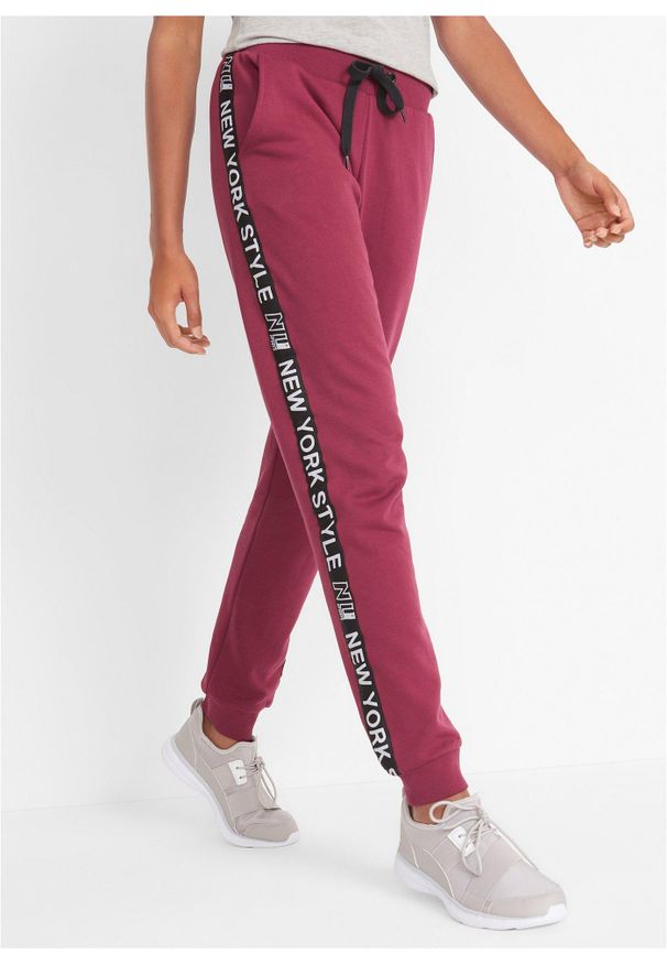 bonprix - Spodnie dresowe ze ściągaczem w talii i u dołu nogawek z napisem. Kolor: czerwony. Materiał: dresówka. Wzór: napisy
