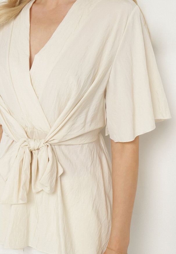 Born2be - Jasnobeżowa Kopertowa Bluzka z Wiskozą Ozdobiona Supłem Tanathria. Okazja: na co dzień. Typ kołnierza: dekolt w serek. Kolor: beżowy. Materiał: wiskoza. Długość rękawa: krótki rękaw. Długość: krótkie. Wzór: aplikacja. Styl: casual