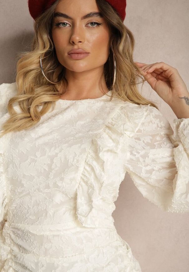 Renee - Jasnobeżowa Marszczona Sukienka z Koronki Zdobiona Falbanami i Półtransparentnymi Rękawami Ziatha. Typ kołnierza: kołnierz z falbankami. Kolor: beżowy. Materiał: koronka. Wzór: aplikacja, koronka. Typ sukienki: dopasowane