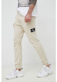Calvin Klein Jeans spodnie męskie kolor beżowy. Kolor: beżowy. Materiał: tkanina, bawełna. Wzór: aplikacja #1