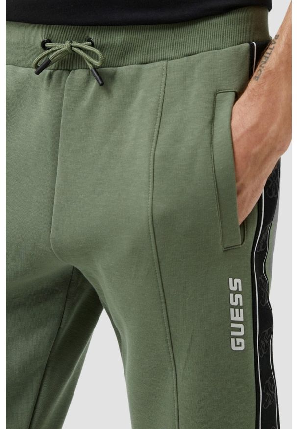 Guess - GUESS Zielone męskie spodnie dresowe z lampasami Mickey. Kolor: zielony. Materiał: dresówka