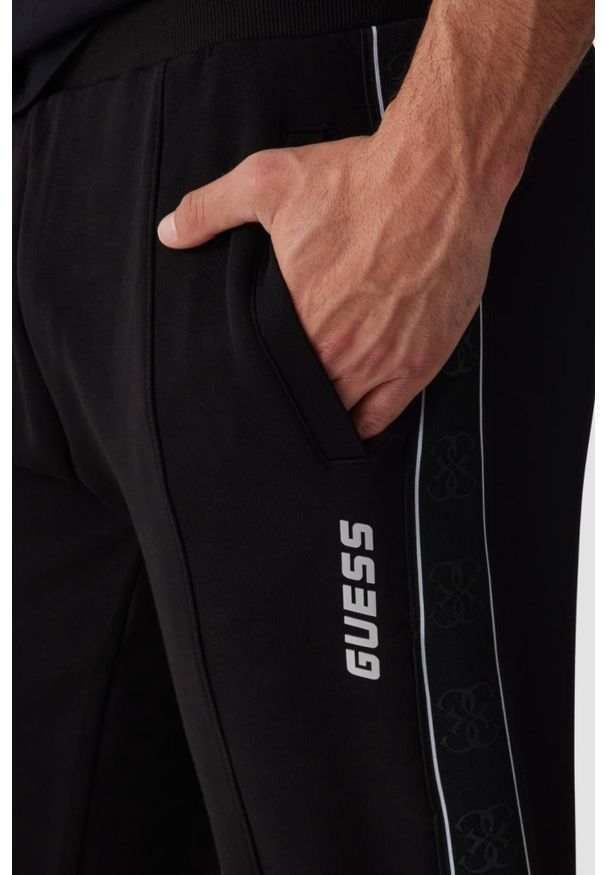 Guess - GUESS Czarne męskie spodnie dresowe z lampasami Mickey. Kolor: czarny. Materiał: dresówka