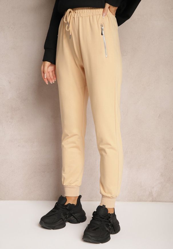 Renee - Beżowe Spodnie Dresowe z Bawełny High Waist Ozdobione Kieszeniami na Suwak Fedela. Stan: podwyższony. Kolor: beżowy. Materiał: dresówka, bawełna. Wzór: aplikacja