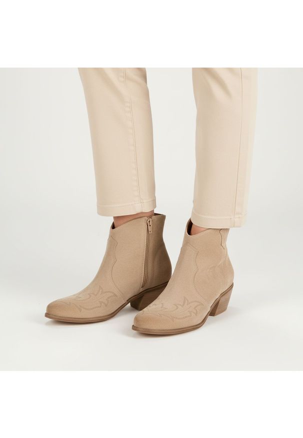 Botki damskie Armodo, cholewka ze skóry naturalnej zamszowej z dekoracyjnym przeszyciem inspirowanym stylem western, stabilny obcas o średniej wysoko. Kolor: beżowy. Materiał: zamsz, skóra. Szerokość cholewki: normalna. Obcas: na obcasie. Styl: elegancki. Wysokość obcasa: średni