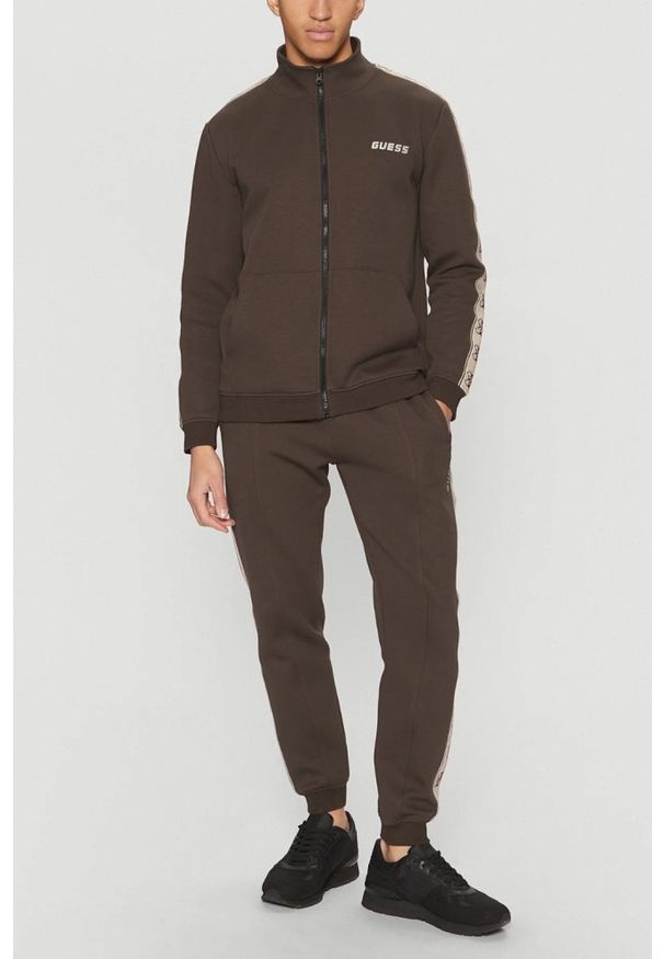 Guess - GUESS Brązowe męskie spodnie dresowe z lampasami Mickey, Rozmiar S. Kolor: brązowy. Materiał: dresówka