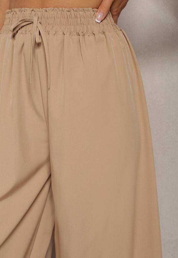 Renee - Beżowe Spodnie High Waist z Szerokimi Nogawkami z Wiskozą Wykończone Gumką w Talii Crisantas. Okazja: na spacer, na spotkanie biznesowe, na co dzień. Stan: podwyższony. Kolor: beżowy. Materiał: wiskoza. Styl: elegancki, biznesowy, casual