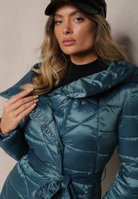 Renee - Niebieska Kurtka Pikowana o Długim Kroju z Kapturem Ozdobiona Wiązaniem w Talii Anselith. Typ kołnierza: kaptur. Kolor: niebieski. Materiał: jeans. Długość: długie. Wzór: aplikacja. Styl: elegancki