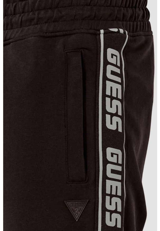 Guess - GUESS Brązowe męskie spodnie dresowe z lampasami New Arlo. Kolor: brązowy. Materiał: dresówka